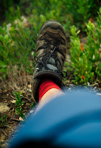 A person wearing brown boots and red socks standing on grass