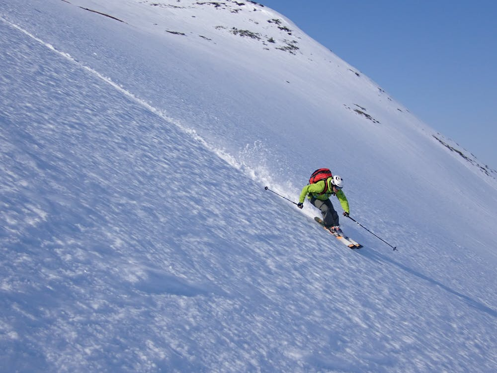 Skier wearing a high-performance ski backpack while descending a snowy backcountry mountain slope.