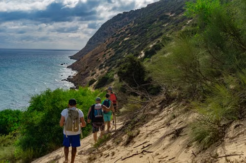 Hikers with backpacks walking a sandy coastal trail overlooking the ocean
