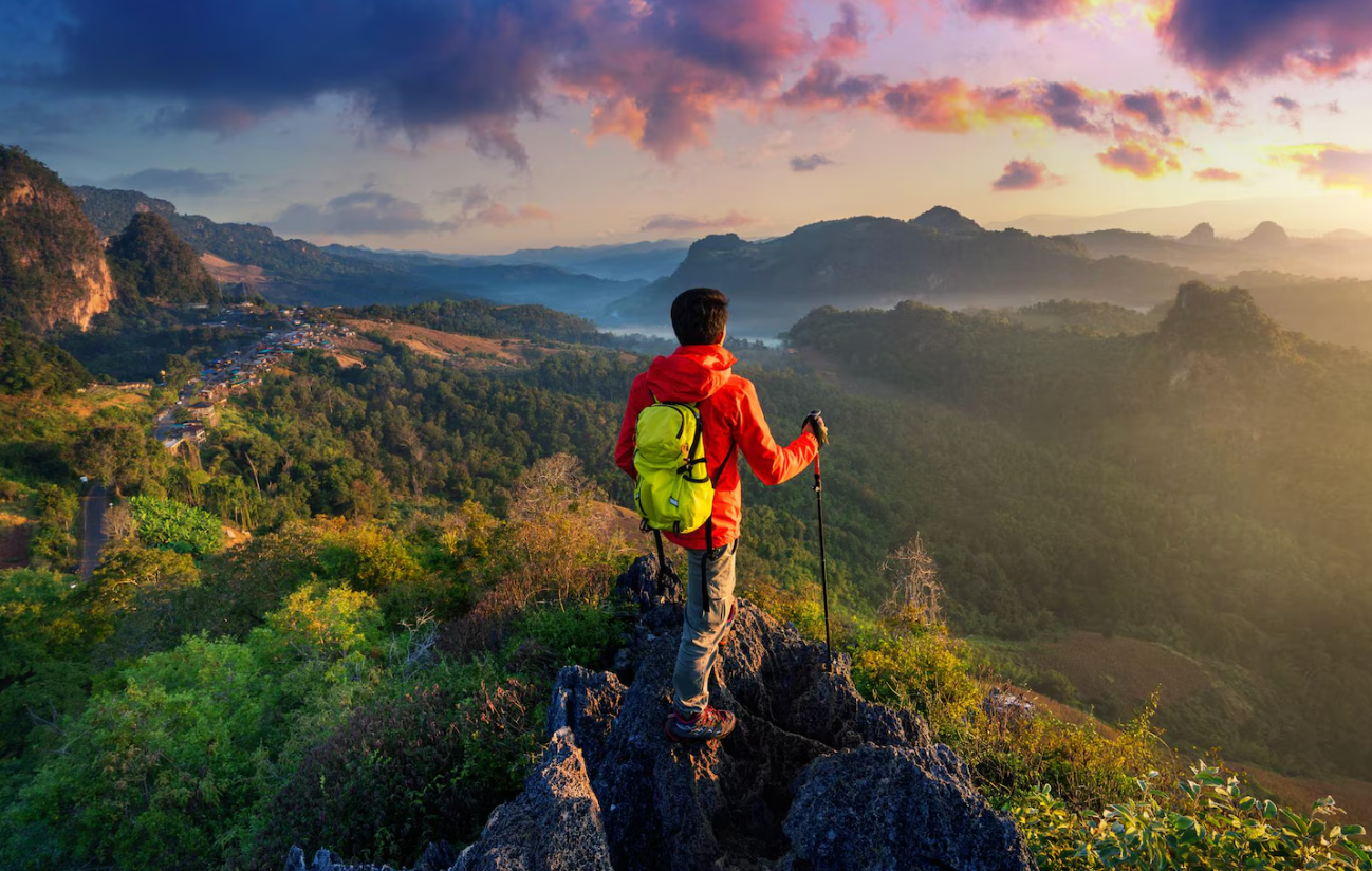 A person wearing a lightweight hiking backpack and standing on a trail, enjoying a scenic view of mountains.